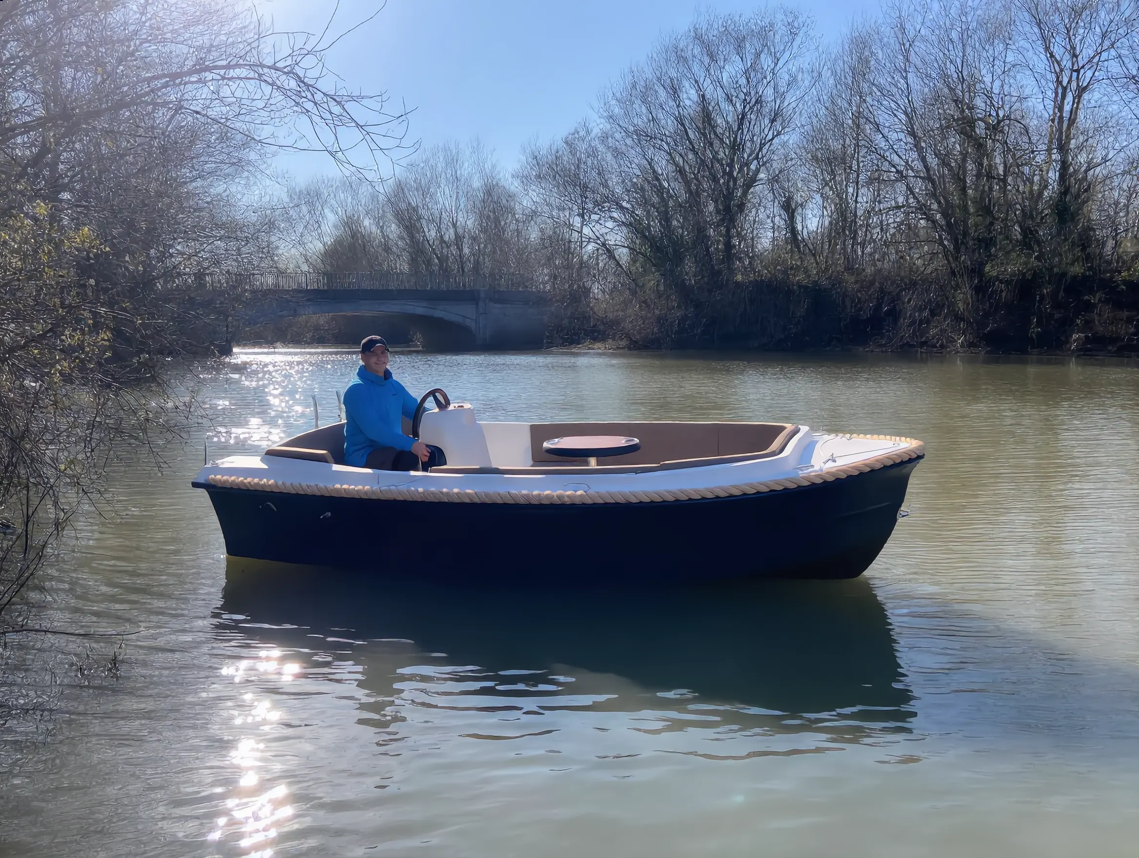 Een luxe sloep met schipper aan het roer, varend over rustig water onder een stenen brug