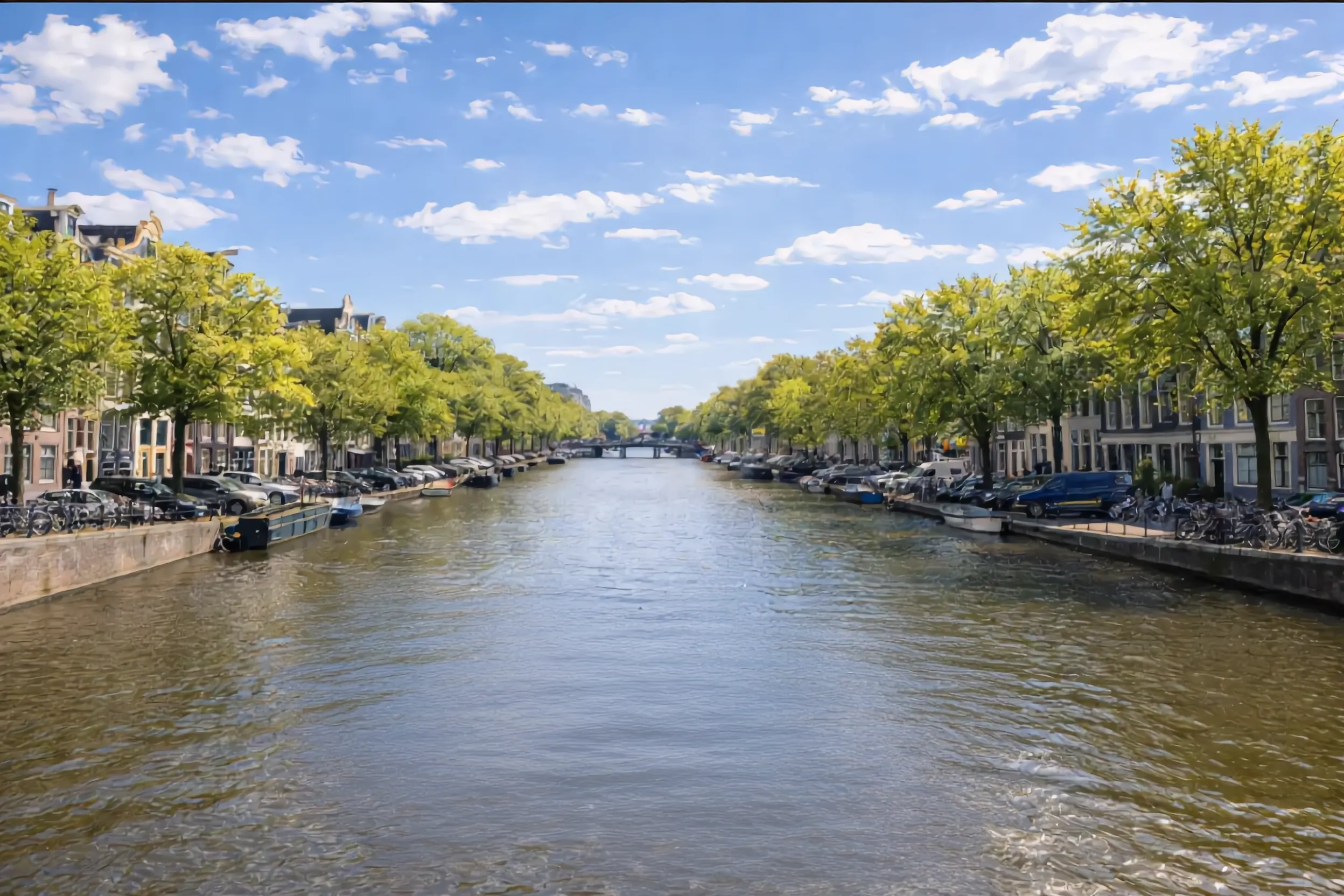 Amsterdamse gracht op een zonnige dag: bomen langs de kade, grachtenpanden en afgemeerde boten aan weerszijden van het water